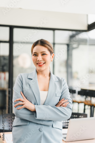 Free Download Young woman in light blue blazer smiling confidently with arms crossed in modern office space - GFXLoad