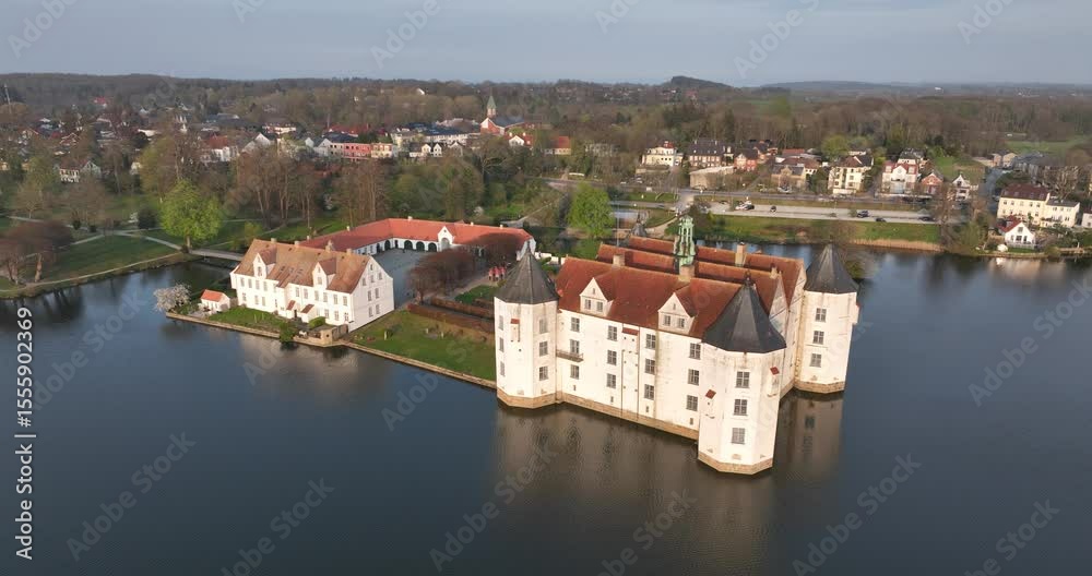 view shows Glucksburg castle with pointed roofs nestled on a lake, connected by a town in Germany