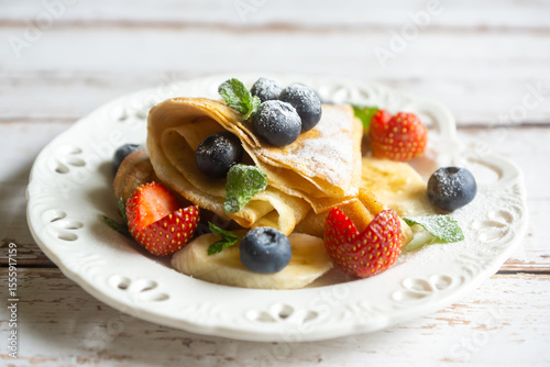 Fototapeta Naklejka Na Ścianę i Meble -  Delicate pancakes with fruits and berries on a wooden table.
