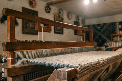 Tapeta Handcrafted wooden loom with wool fabric partially woven, situated in cozy rustic interior with folk patterns on walls