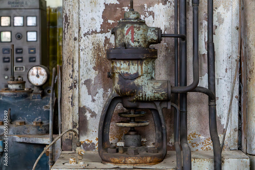 Wallpaper Mural Old industrial valve covered in rust, mounted on a weathered wall in a technical room. Control panels and pressure gauges visible in the background, evoking a retro industrial atmosphere. Torontodigital.ca