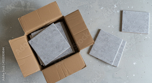 Cardboard box with ceramic tiles unpacked on grey floor  
