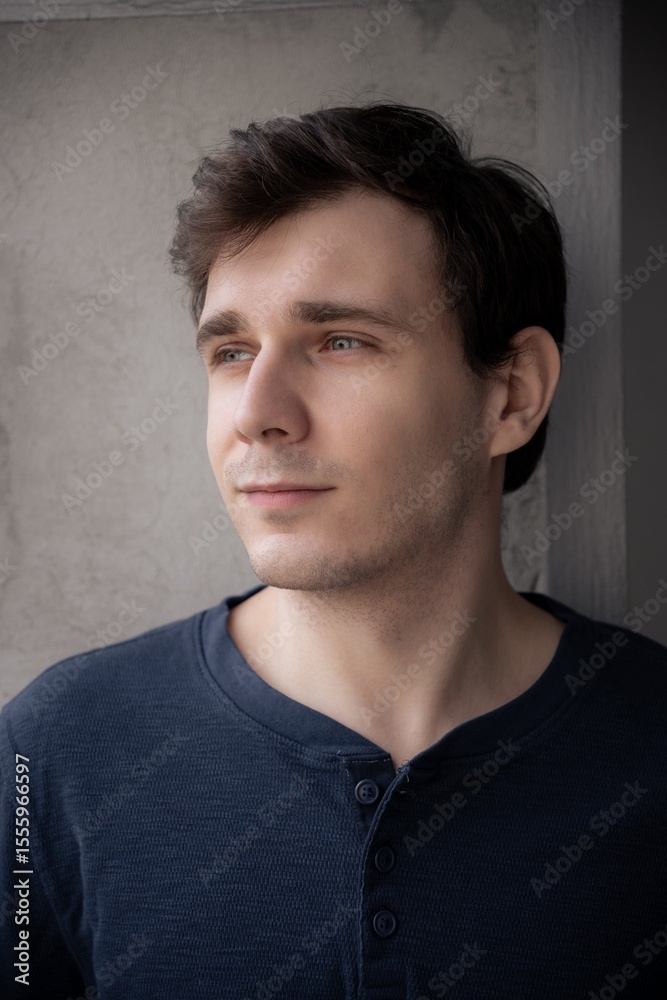 Obraz premium Man gazing thoughtfully by a window in soft indoor lighting, moments captured in contemplative silence during a quiet afternoon