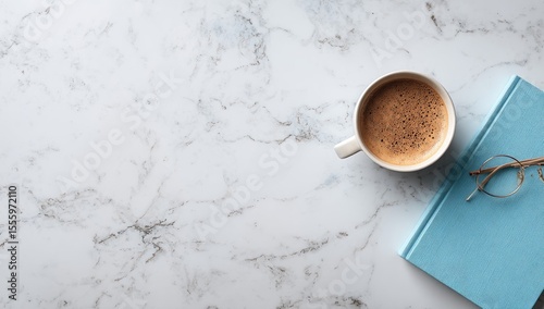 Overhead view of a coffee cup, book, and glasses on a marble surface