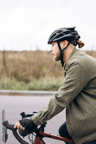 Young bearded man in helmet and casual clothes riding bicycle to work.