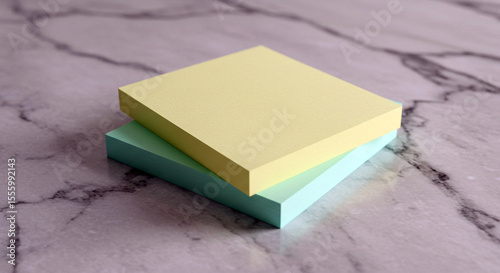 Two stacks of pastel colored sticky notes yellow and light green placed on a textured marble surface with a shallow depth of field