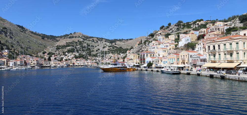 Naklejka premium Seaside Greek Village – Symi Island Harbor with Boats and Hillside Homes
