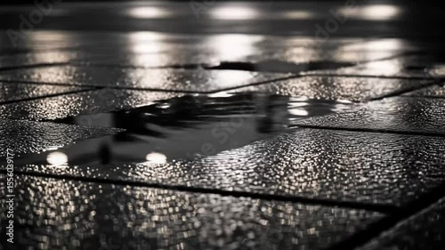 Close-up view of a wet city pavement at night, reflecting lights and figures.