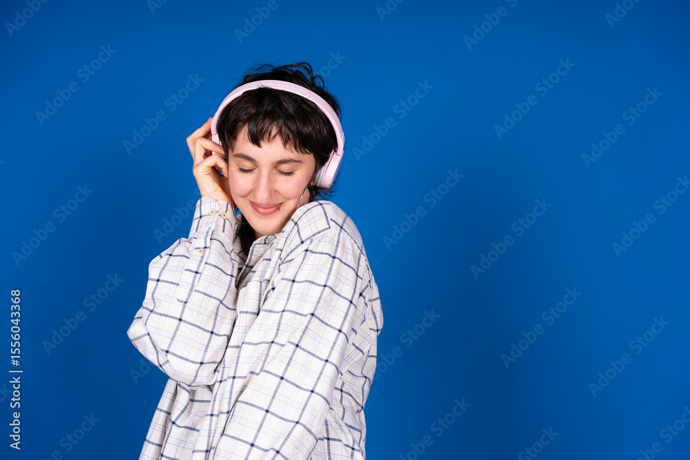 Fototapeta premium Young woman enjoying music with headphones on blue background