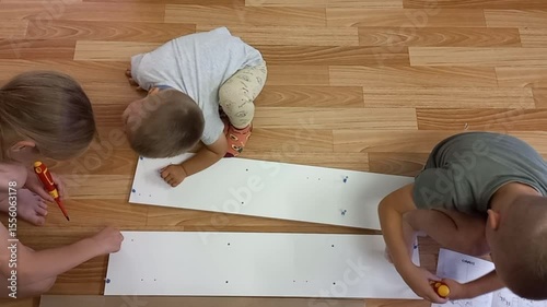 Three children assemble furniture on the floor indoors