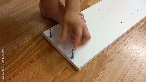 Child assembling furniture with hands on wooden floor at home  