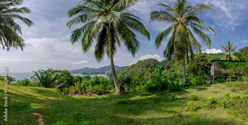Views through lush green trees and palms over looking Kata and Kata Noi on the beautiful island of phuket in Thailand with lush green mountains and turquoise blue waters of the Andaman Sea