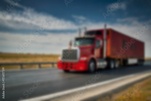 Blurry photo of container truck carrying large containers on highway with beautiful sunset.