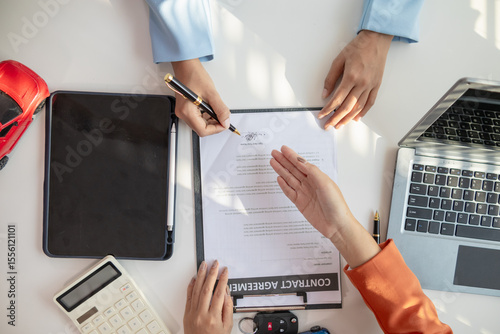 Asian businesswoman agreeing to sign a contract to buy a car from a car dealer for business use. Image of a businesswoman and a car dealer agreeing to sign a contract to buy a car from dealer.