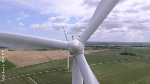 Close-up of wind turbine blades against farmland and cloudy sky, renewable energy source in rural landscape
