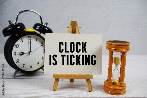 Clock is Ticking text with hourglass and alarm clock on wooden background photo