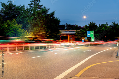 Light trails on a street and junction close to an overpass in the evening, where the sky is not yet completely dark.