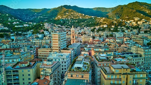 Wide aerial skyline of Rapallo city nestled between emerald Ligurian mountains and Mediterranean coast with basilica campanile as focal point, Italian Riviera, Italy	