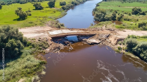 Damaged Bridge Over River.  Aerial view of a partially collapsed bridge over a river, with construction debris and exposed supports.  Surrounding landscape shows fields and vegetation