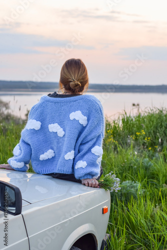 Woman in Cloud Sweater Enjoying Sunset View by the River. Peaceful Rural Moment	