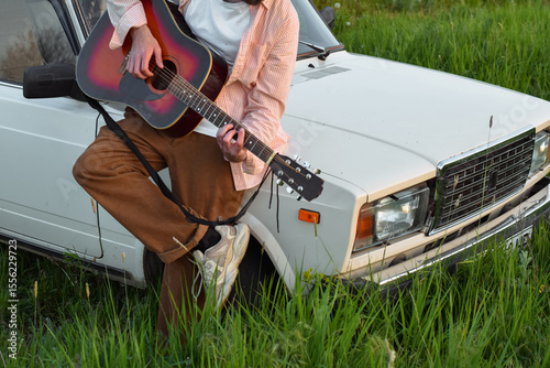 A man is playing on guitar near the car