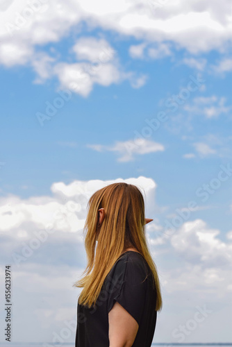 Girl with elf ears is standing against blue sky with white clouds