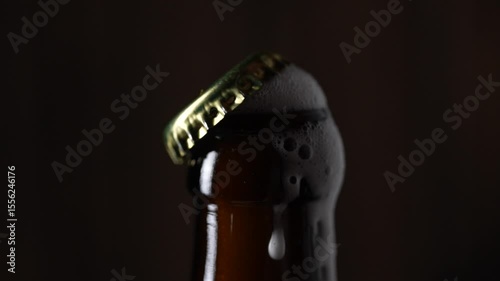 Men's hands open bottle of beer on black background, close up. Beer foam coming out of brown beer bottle, slow motion