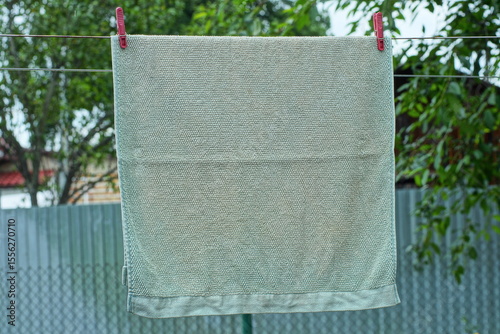 one large clean stylish gray with patterns soft home wet cloth washed towel hanging on a rope with red plastic clothespins during daytime outdoors in summer