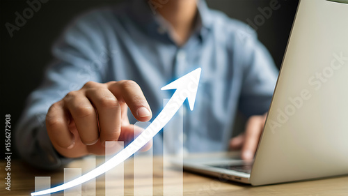Person interacting with a digital graph showing upward growth and a laptop computer