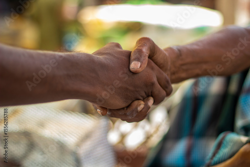 A white boy and a black boy are shaking hands and the background behind them is blurred.