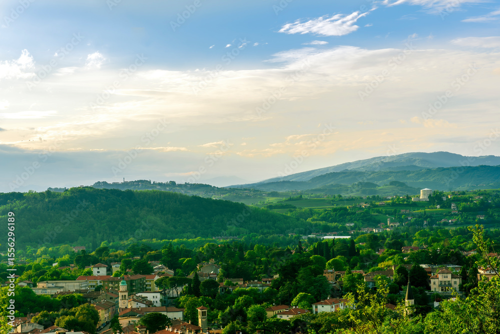 Obraz premium travel summer view from hill to a nice european town with amazing buildings, green hills and mountains with amazing cloudy evening sky on background
