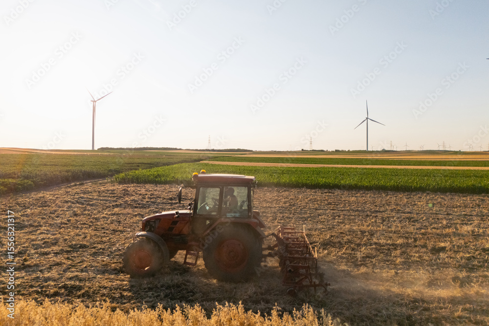 Obraz premium Agricultural tractor is working on the field with wind turbines. Aerial view