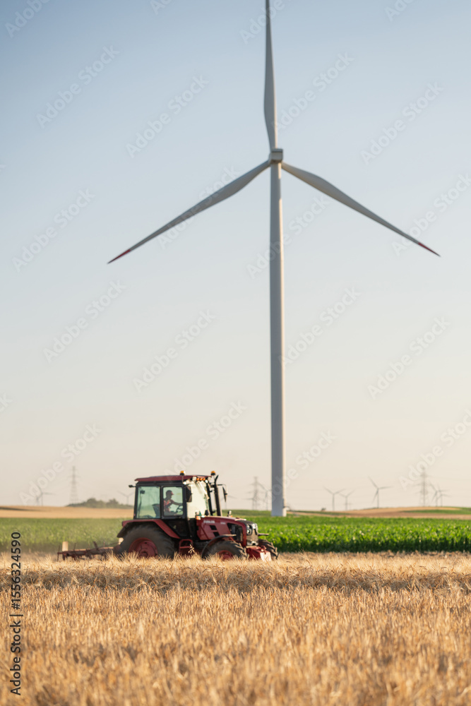 Fototapeta premium Agricultural tractor is working on the field with wind turbines