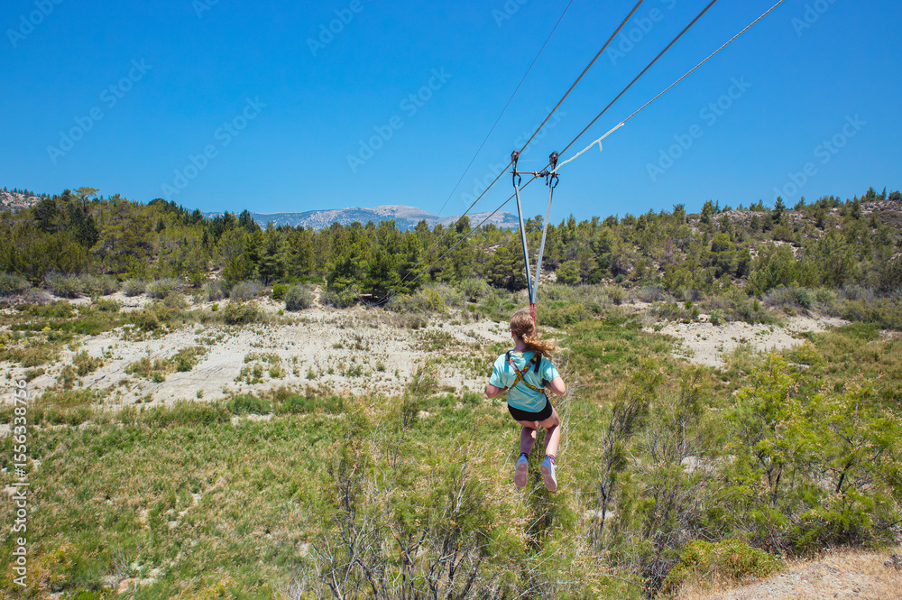 Obraz premium Girl child using zip line at Rhodescape Park at the artificial lake of Apolakkia in Rhodes, Greece.