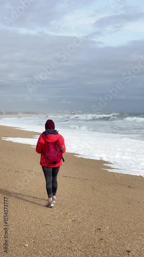 Slow motion 4K vertical footage female with red backpack walking by wide sandy beach at Aguda settlement near Porto, Portugal. Environment, travelling, recreation concept.