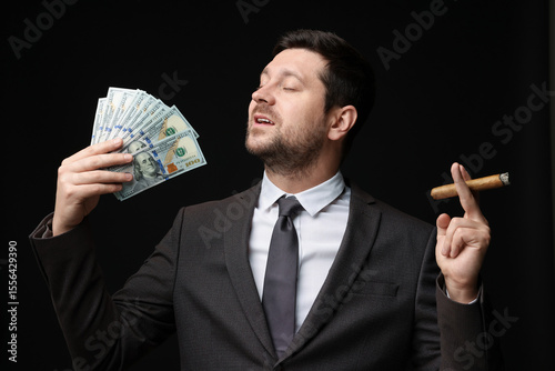 Fényképezés Greedy banker with dollar banknotes smoking cigar on black background