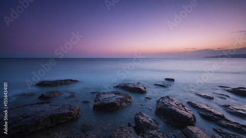 Captivating Twilight View of Rocky Shore With Calm Waves and Colorful Sky at Sunset by the Ocean