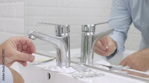 Blurred Shooting with a Sick and Suffering Man in Front of the Bathroom Mirror taking from the Sink Medical Pills.