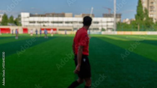 A referee in a red shirt watches players during a football match
