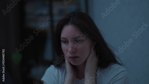  Young adult woman sitting on the bed in the middle of the night suffering from neck pain rubbing her hands. Concept of spine problems due to bad sleeping position and bad pillow