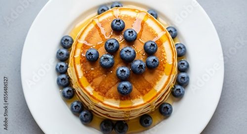 Stack of pancakes with blueberries and syrup on a white plate from an overhead perspective view