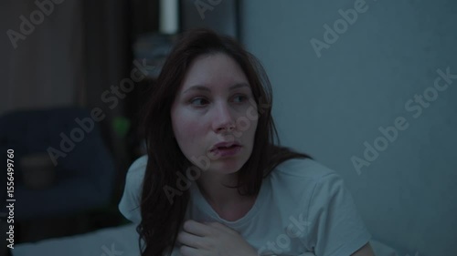 A young adult woman sits on a couch in the middle of the night, nervously twirling her hair. Panic attacks and mental health