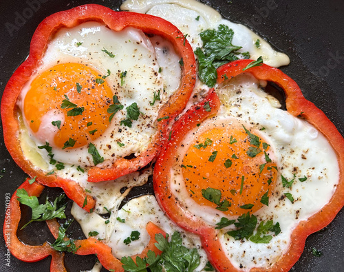 Sunny side up eggs fried in vibrant red bell pepper rings with extra virgin olive oil, topped with fresh parsley for a wholesome and colorful breakfast.