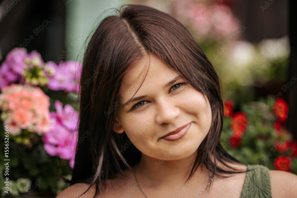 Portrait of a young woman smiling softly with flowers in the background. Her dark hair is blowing in the wind and she is wearing a silver necklace. Portrait of a young woman smiling softly with flowers in the background. Her dark hair is blowing in the wind and she is wearing a silver necklace.