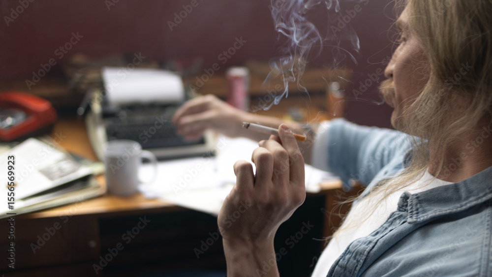 © Ulia Koltyrina - Moody close-up of a man smoking at his desk, atmospheric lighting highlighting addiction and fatigue.