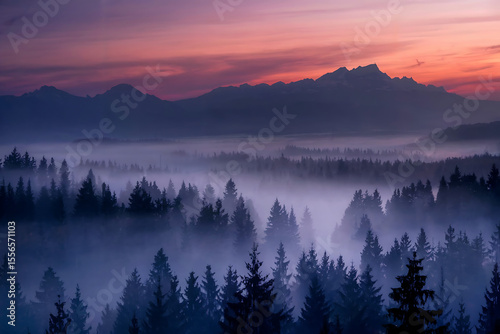 The sunset paints the sky over a misty mountain forest, creating a serene landscape.