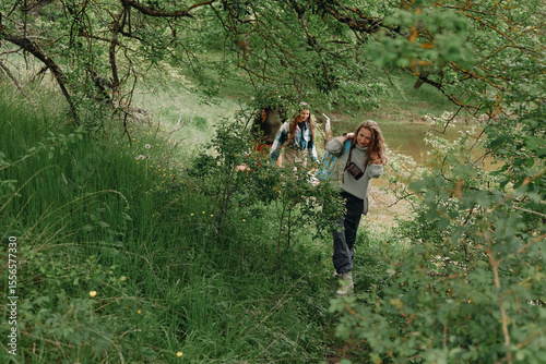 Active middle age woman hiking through lush green forest trail with another older woman, enjoying health, wellness, and community in nature.