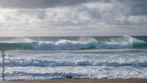 Obraz na plátně Horizontal line of turquoise waves rises along the horizon in windy ocean scene with overcast sky
