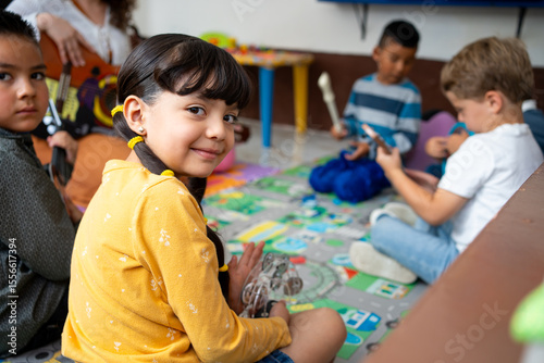 Kindergarten children smile while playing musical instruments with their teacher in a colorful classroom. A diverse preschool learning environment promotes sound exploration and early creativity