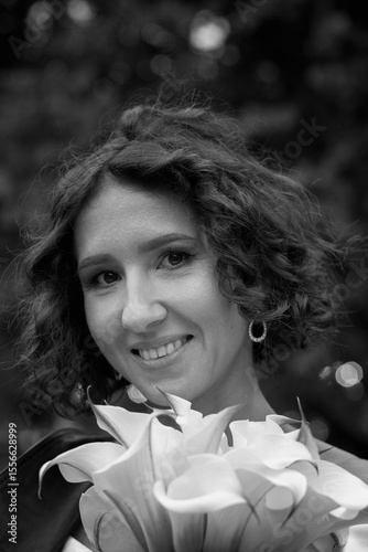 Black and white portrait of a smiling bride wearing a leather jacket and holding flowers, captured in a candid outdoor moment.  Smiling Bride in Leather Jacket — Black and White Portrait
